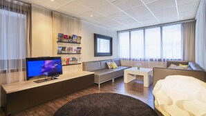 A modern living room with a flat-screen TV, a sofa, a coffee table, and a patterned ottoman.