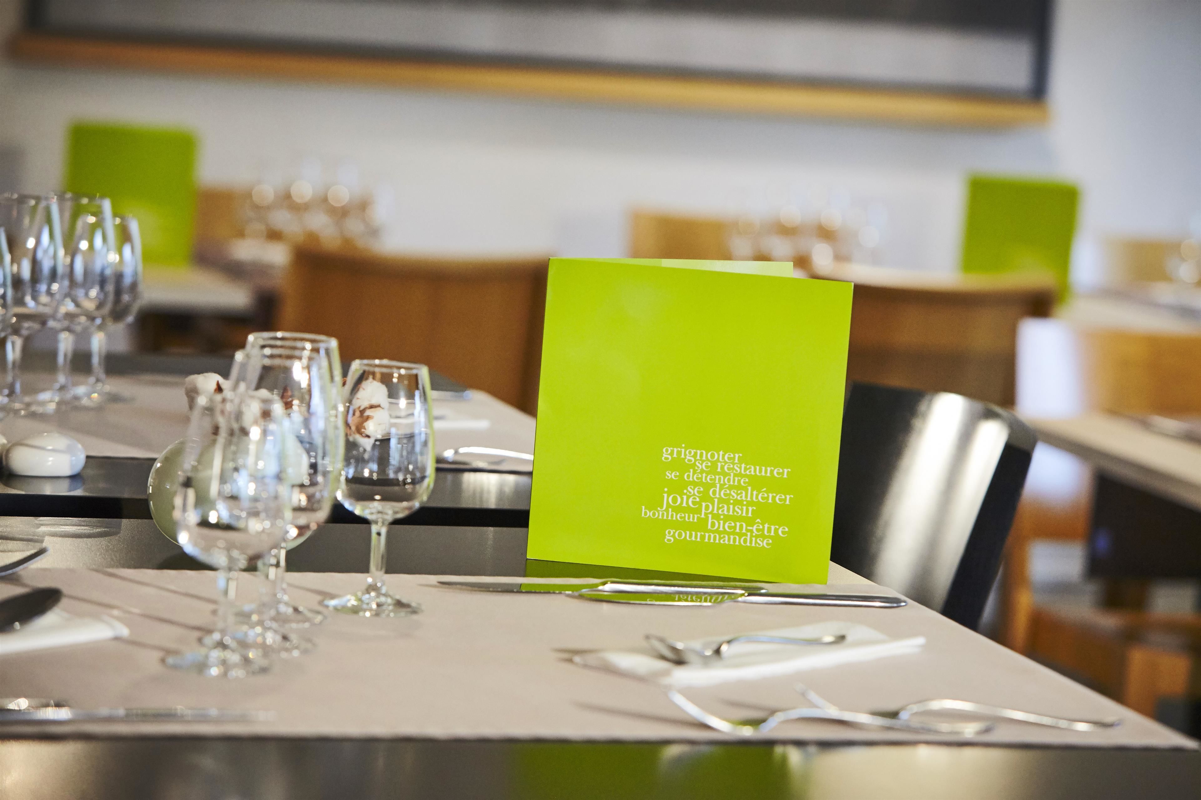 Une table à manger dressée avec des verres à vin et un menu vert.