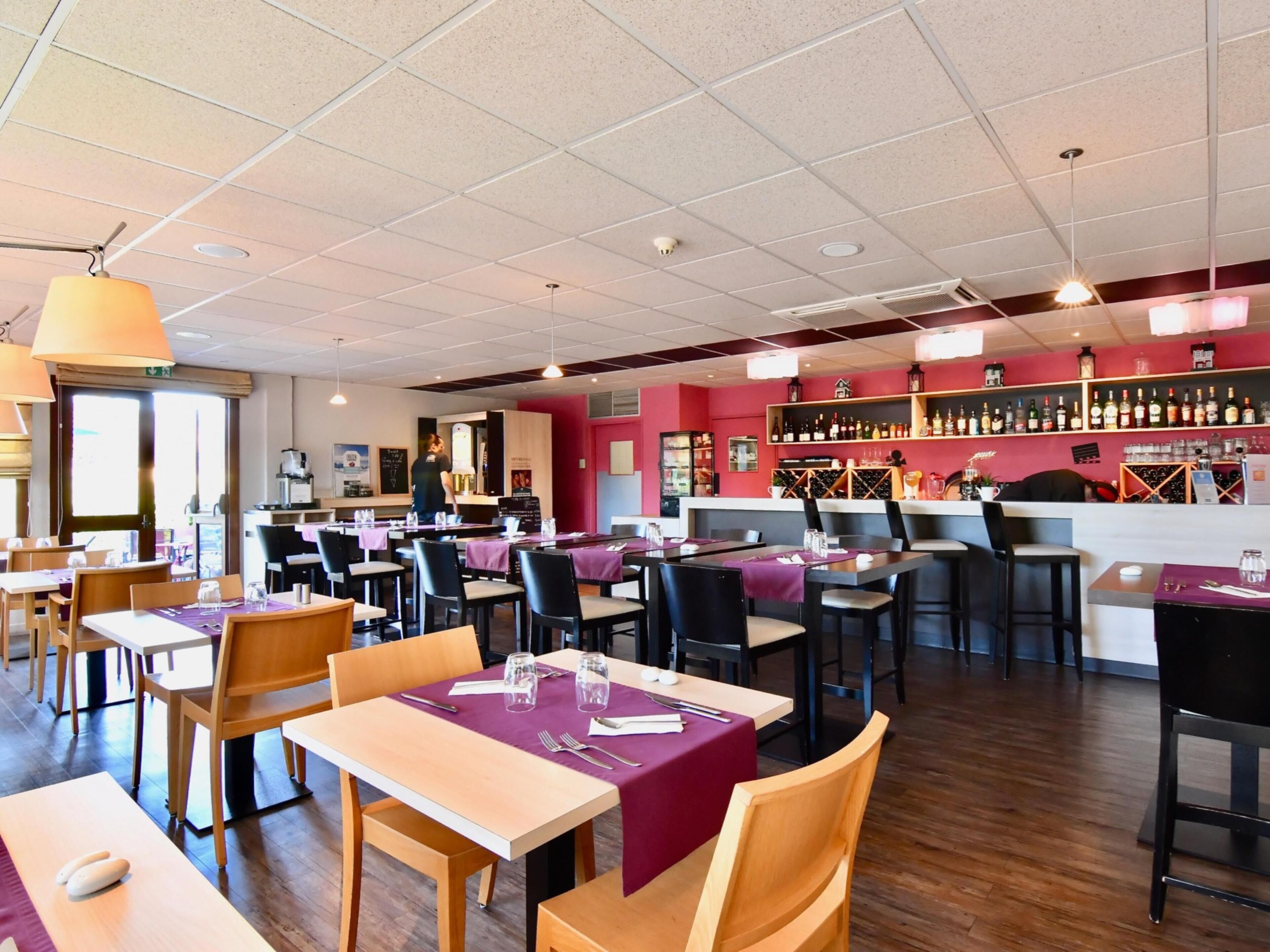 L’intérieur d’un restaurant présente plusieurs tables, des chaises, un bar avec des étagères remplies de bouteilles et un plafond doté d’un éclairage encastré.