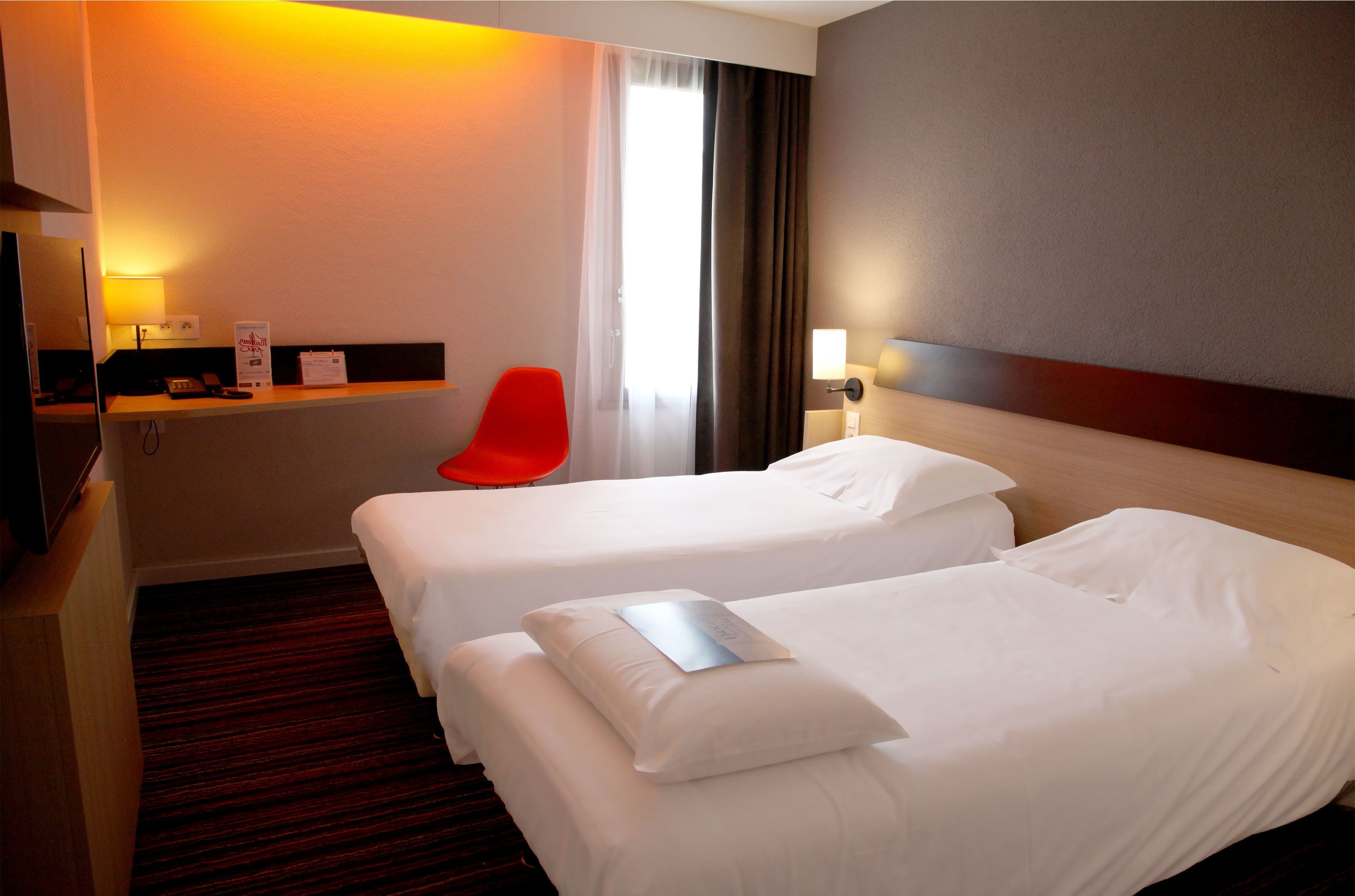 Una habitación de hotel con dos camas, un escritorio con silla, televisión y ventana con cortinas.