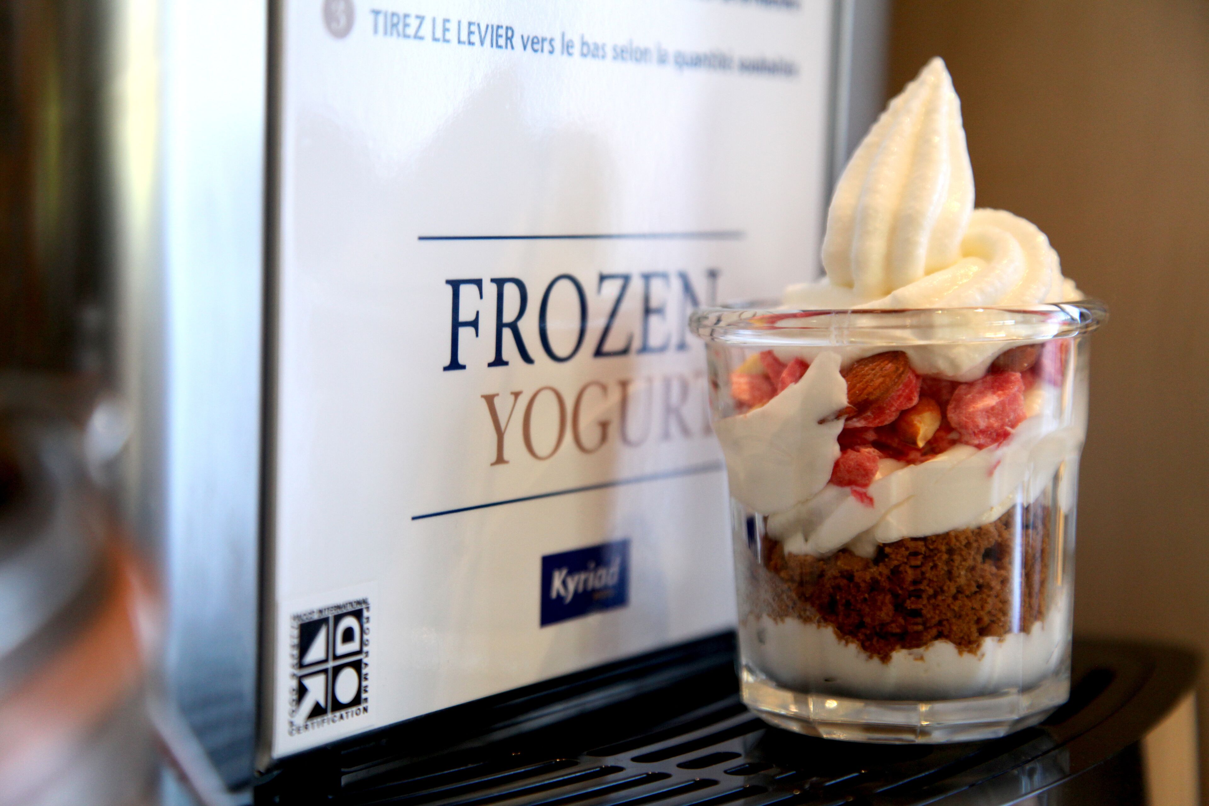 A glass dessert with whipped cream and strawberries, placed in front of a sign for frozen yogurt.