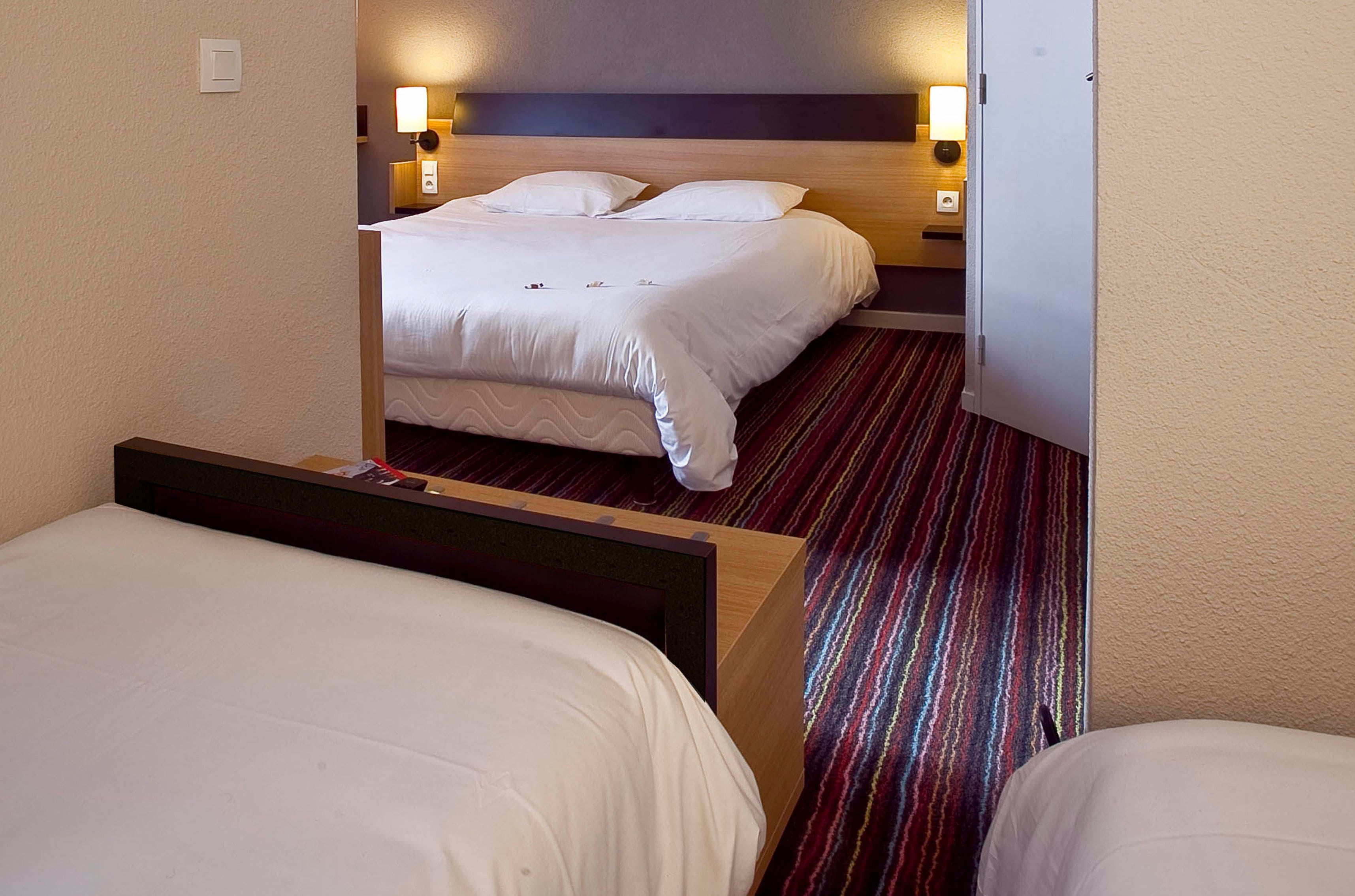 Ein Hotelzimmer mit zwei Betten, einem Holzkopfende, einem Streifenmuster-Teppich und Nachttischlampen.