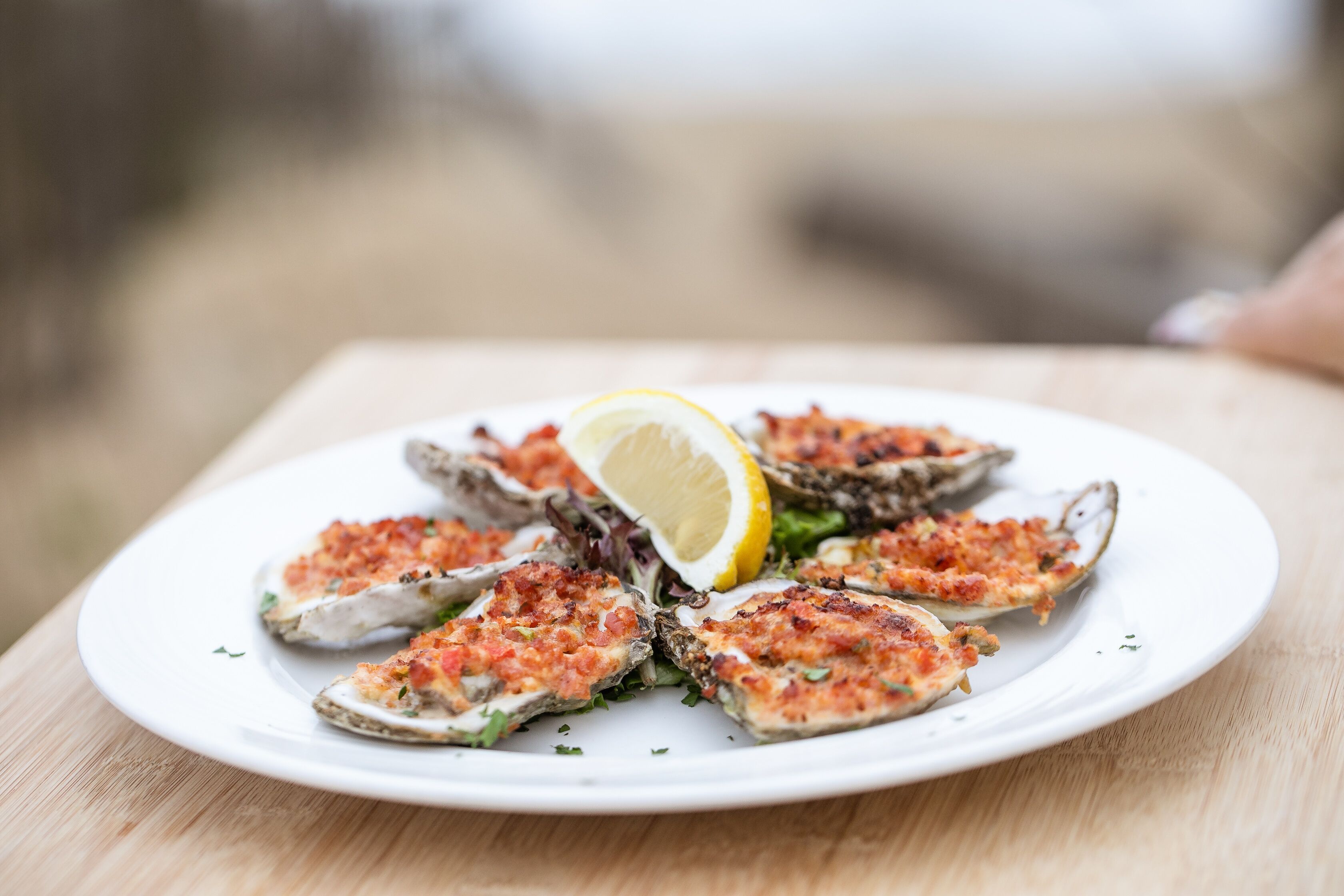 A plate of grilled oysters with a lemon wedge on a wooden table.