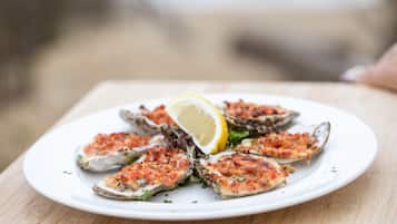 A plate of grilled oysters with a lemon wedge on a wooden table.