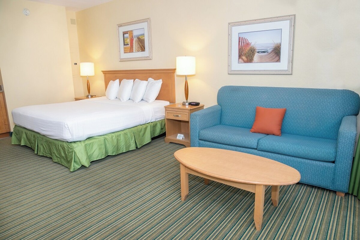 Una habitación de hotel con una cama, un sofá azul, una mesita y dos lámparas.