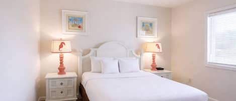 A bedroom with a white bed, two nightstands, two lamps, and two framed pictures on the wall.