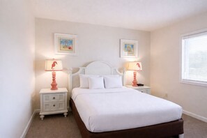 A bedroom with a white bed, two nightstands, two lamps, and two framed pictures on the wall. - Sea Ranch Resort (Kill Devil Hills)
