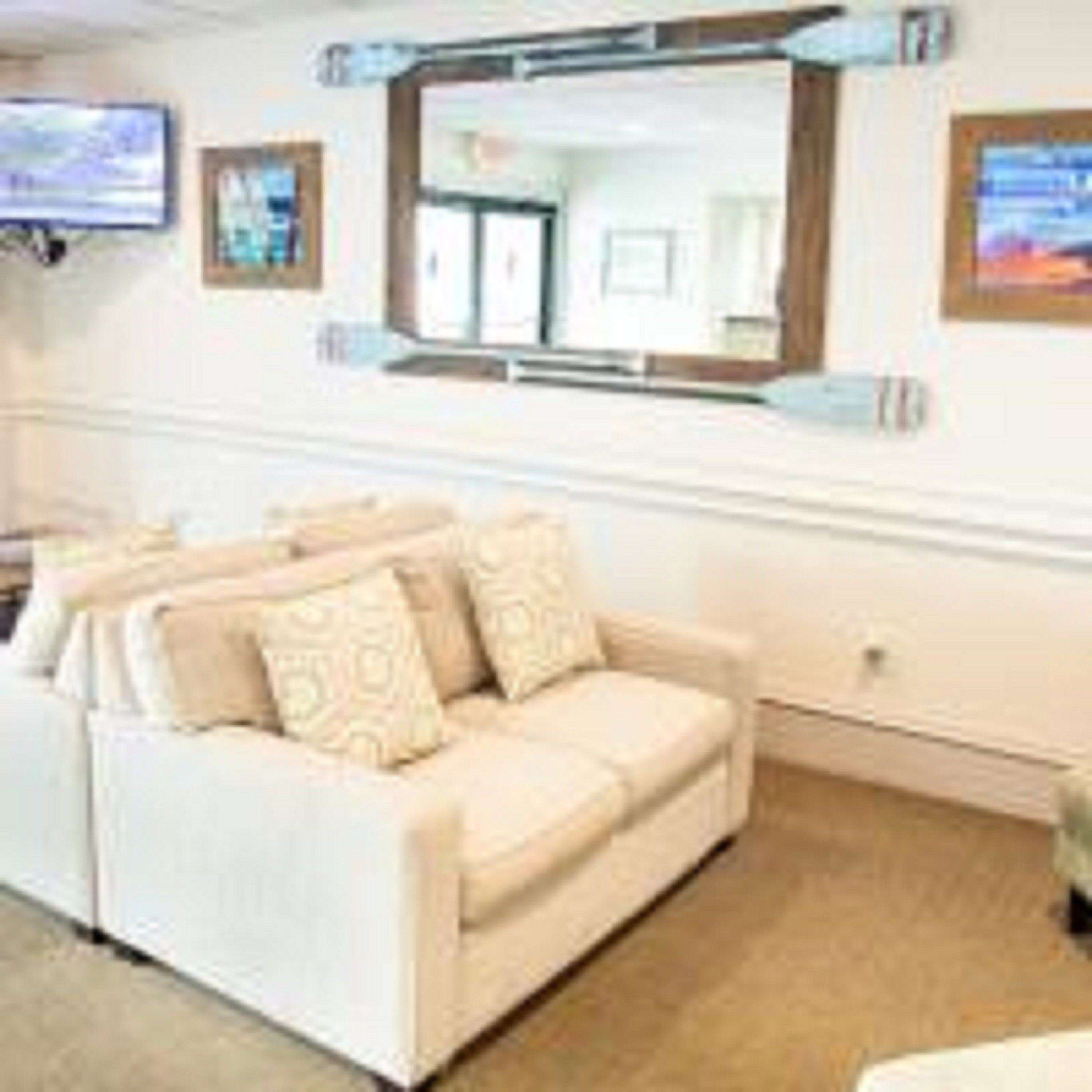 A beige sofa with patterned cushions in a room with a large mirror above it.