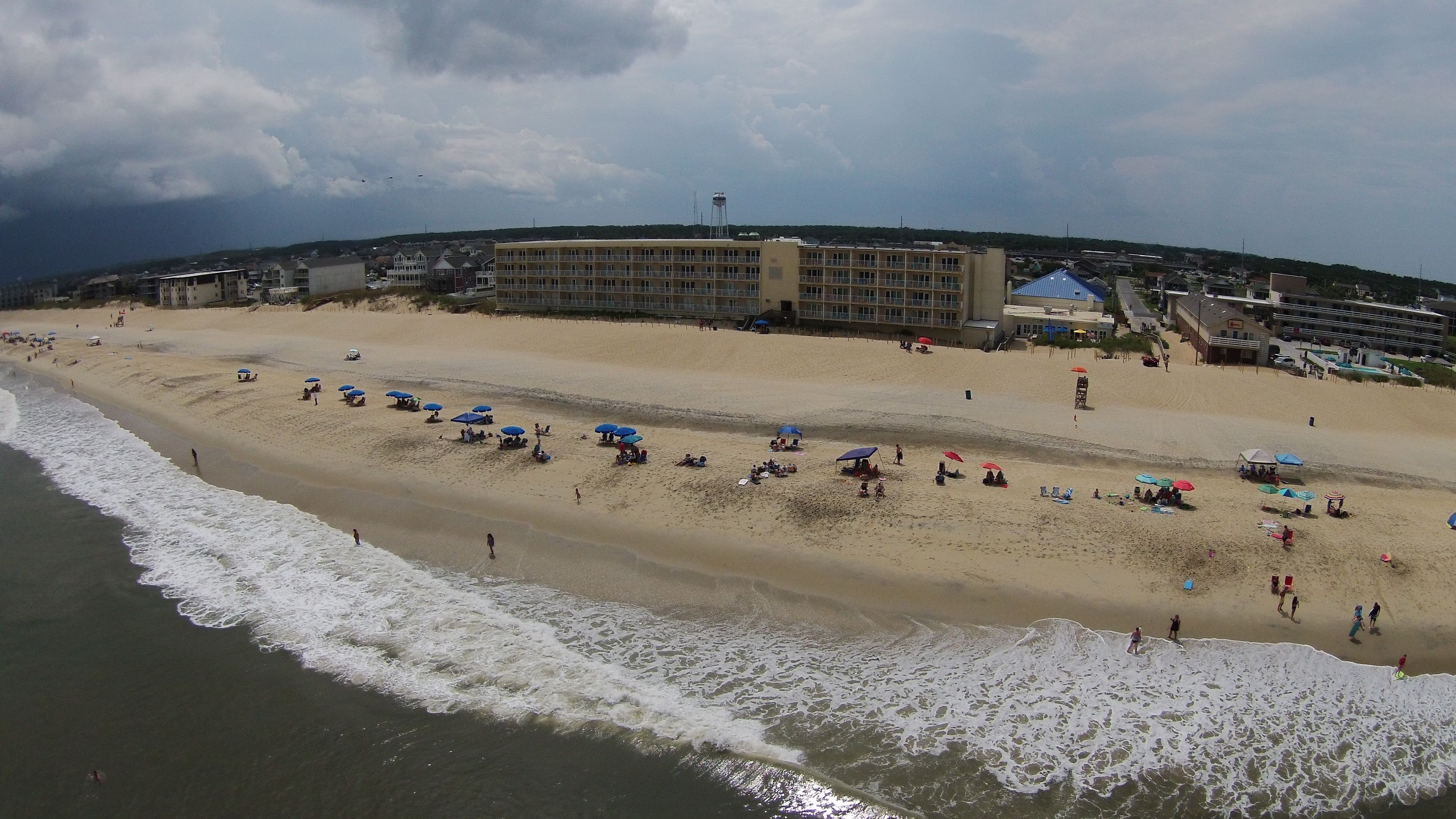 A beach with umbrellas and people, a large building in the background, and a water tower.