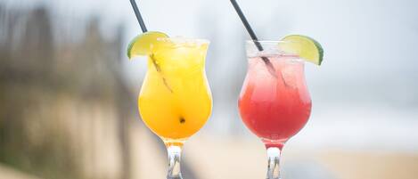 Deux cocktails sur une surface en bois, avec une plage floue en arrière-plan.