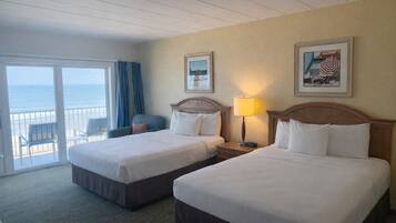 Habitación de hotel con dos camas, un balcón con vista al océano y una silla.