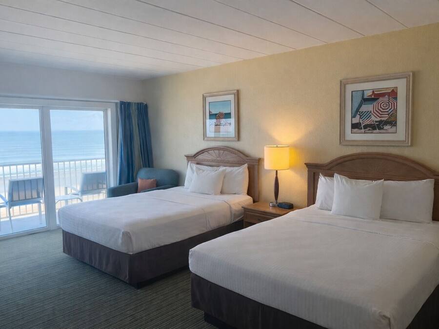 Habitación de hotel con dos camas, un balcón con vista al océano y una silla.
