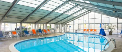 An indoor swimming pool with clear blue water, surrounded by lounge chairs and a glass ceiling.