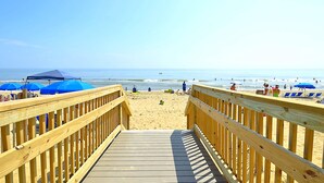 Una passerella in legno che conduce a una spiaggia con ombrelloni blu e persone.