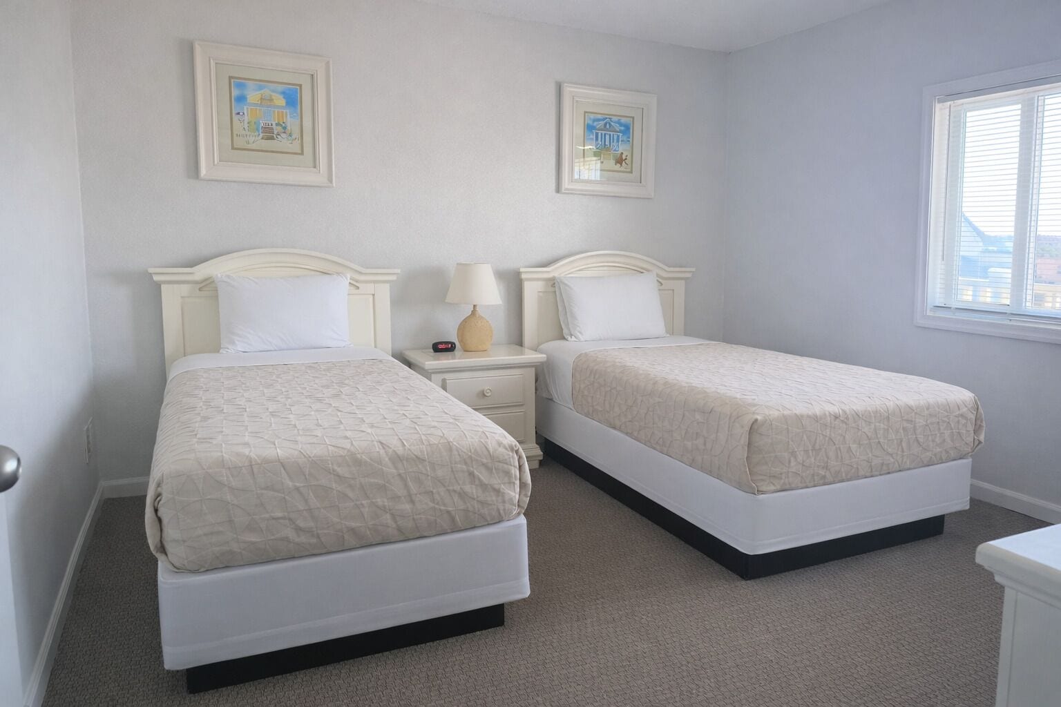 A bedroom with two beds, a nightstand with a lamp, and framed pictures on the wall.