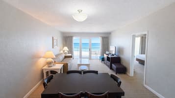 A hotel room with a dining area, a sofa, a TV, and a balcony with a view.
