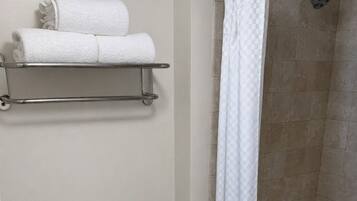 A bathroom with a toilet, a shower with a checkered curtain, and a shelf with towels.