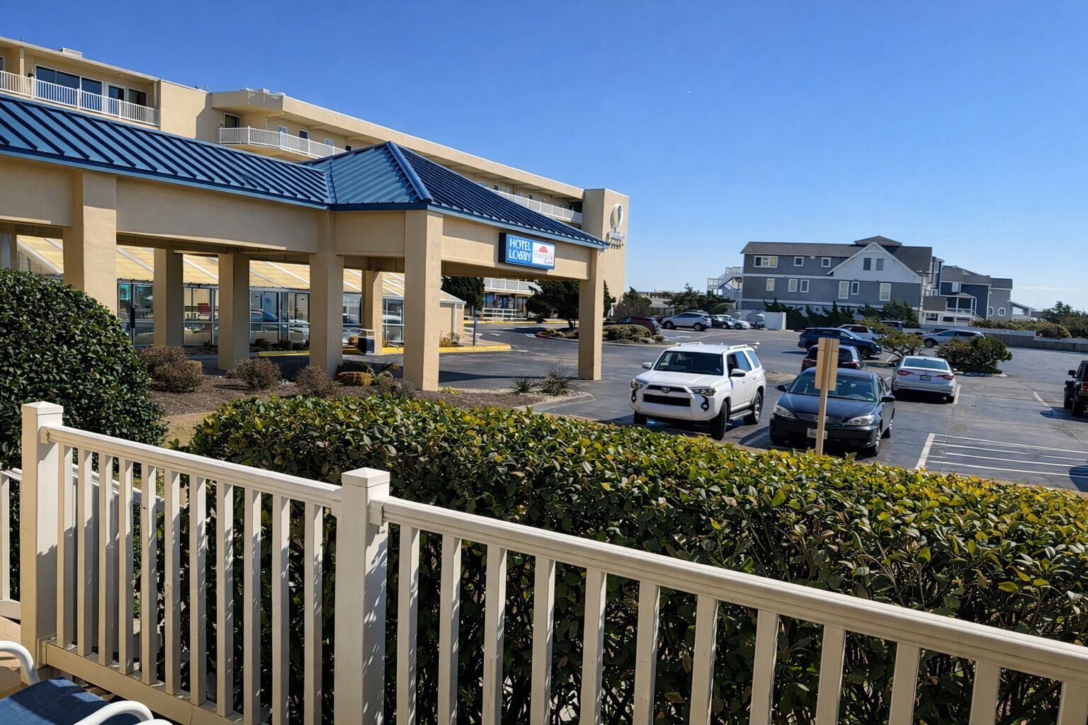 Un hotel con techo azul, vestíbulo visible y estacionamiento con varios coches.