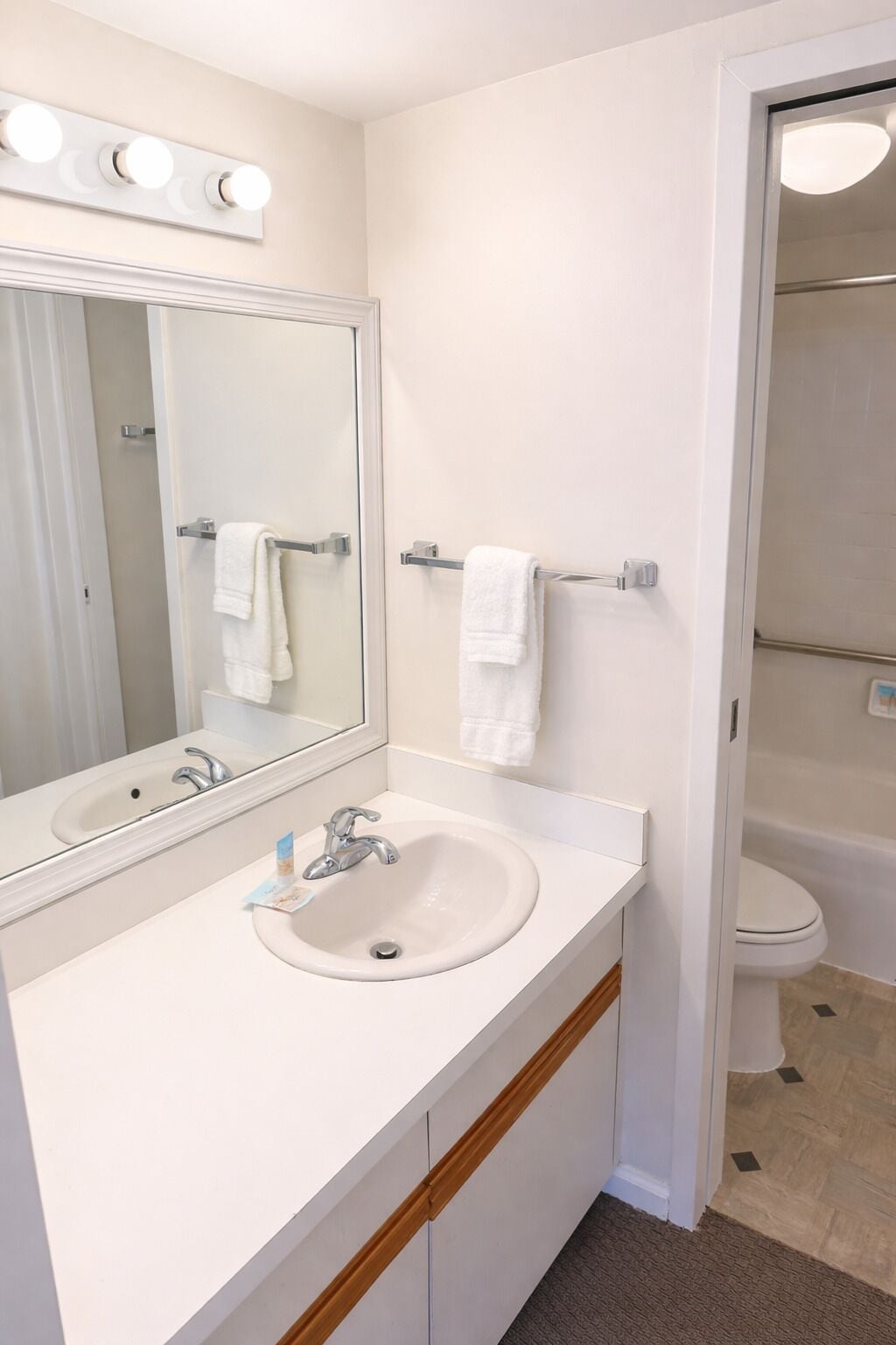 Un baño con lavamanos, espejo, toallero y retrete.