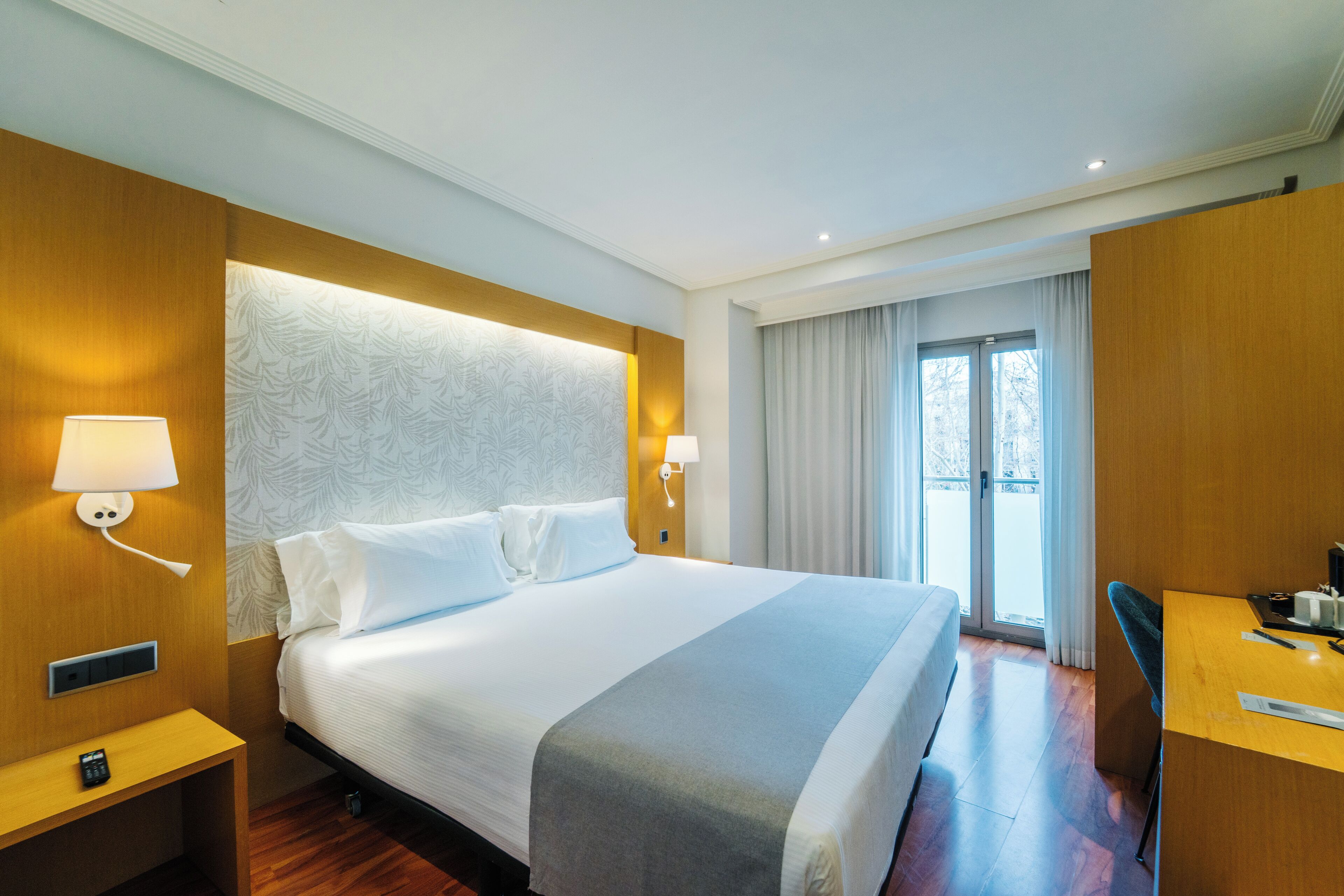 Een hotelkamer met een groot bed, nachtlampjes, een bureau en uitzicht op de omgeving.