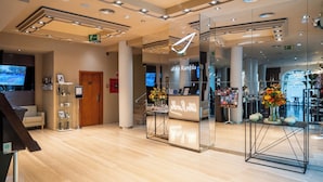 En moderne hotellobby med en receptionsdisk, en trappe og et stort spejl der afspejler indretningen.