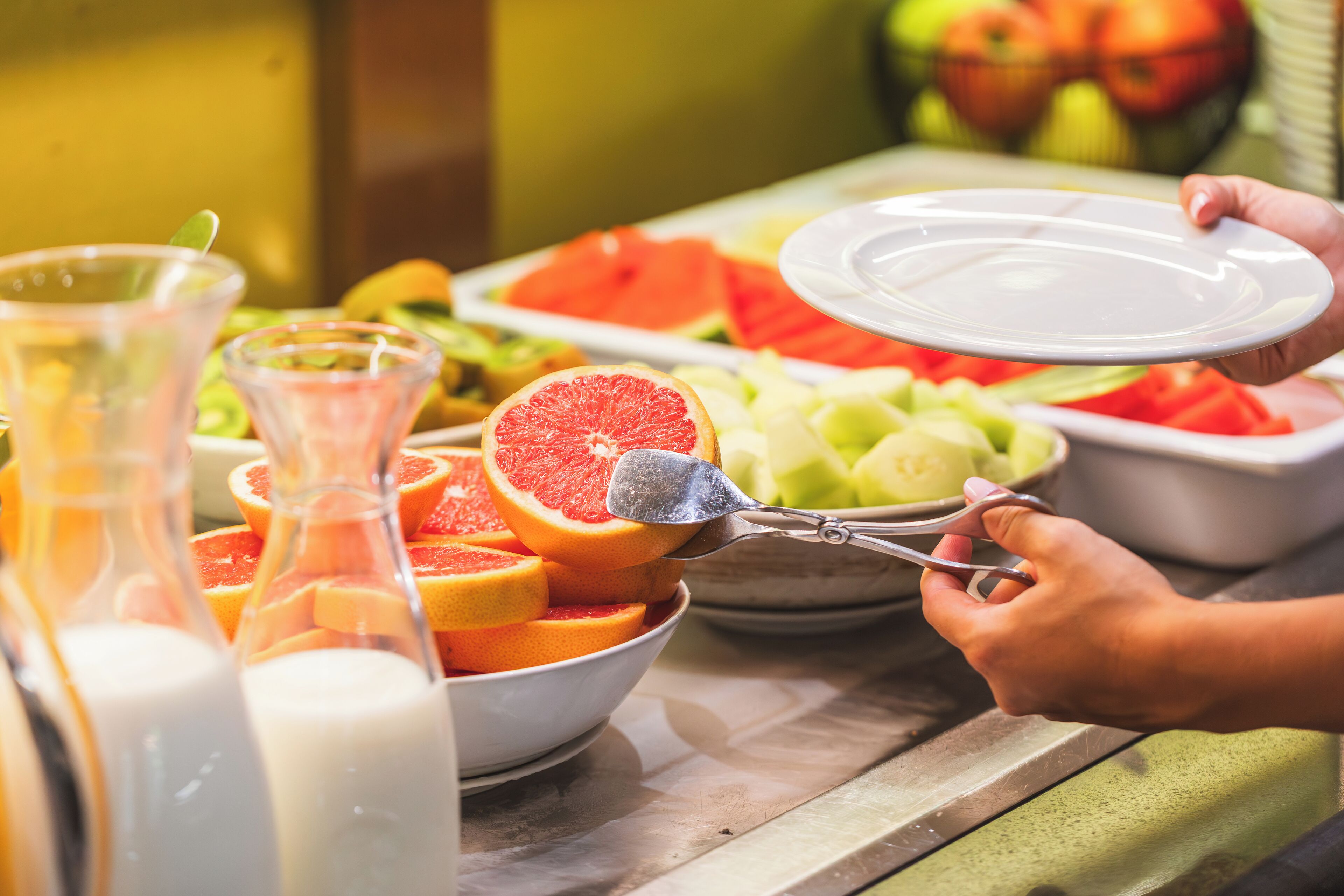 Un buffet proposant une variété de fruits, et une personne se servant elle-même.