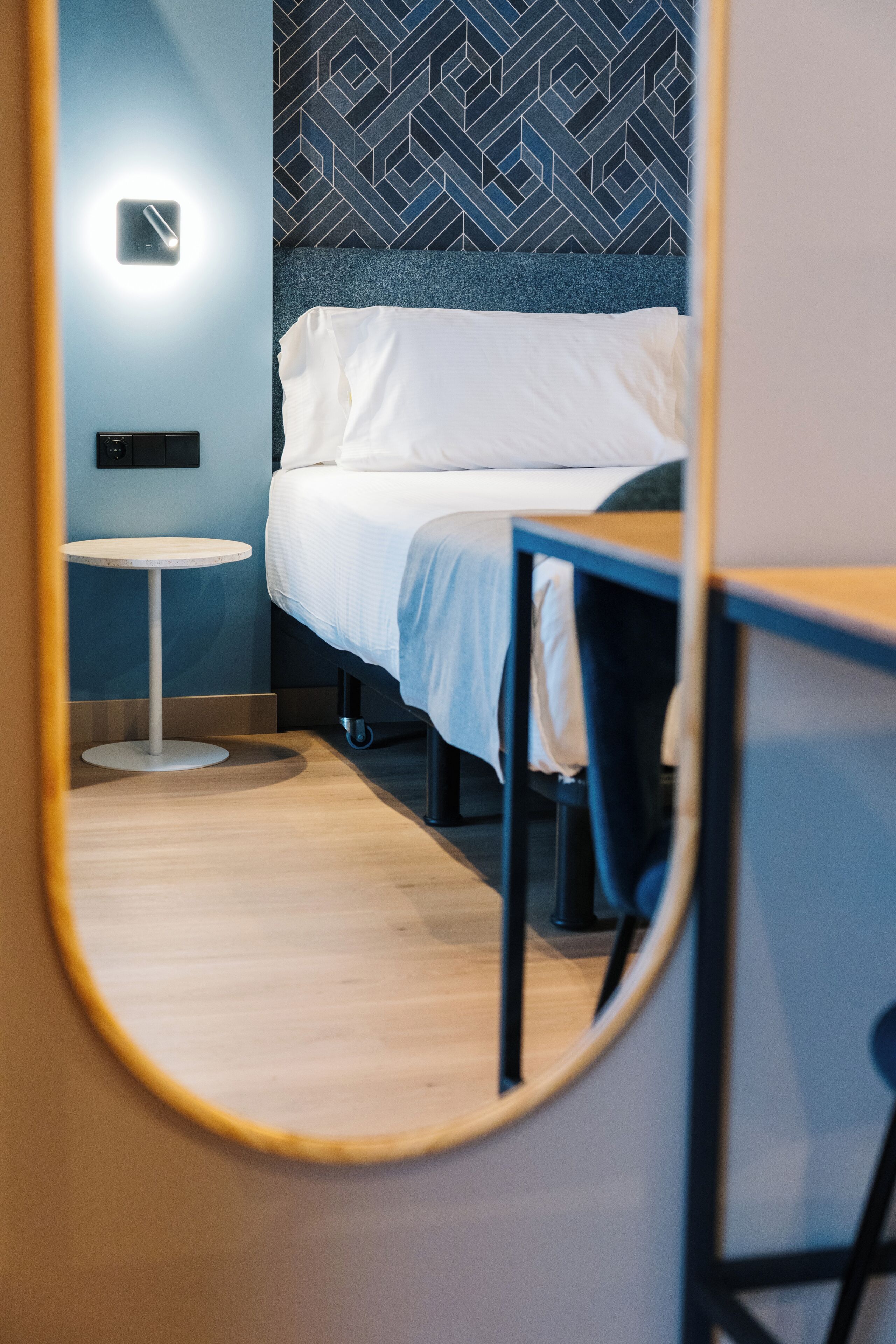 A modern hotel room with a neatly made bed, a small round table, and a patterned wall.