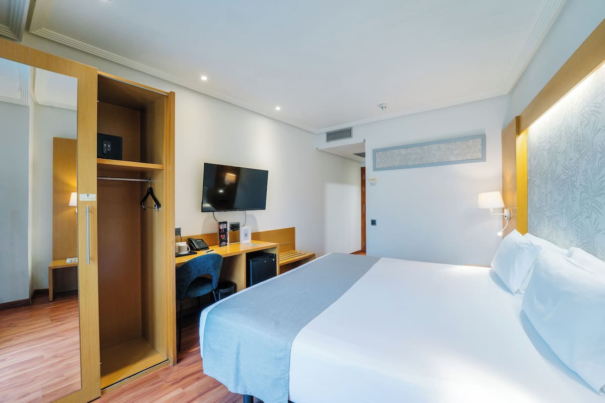 Et hotelværelse med seng, skrivebord med computer, TV og garderobeskab.