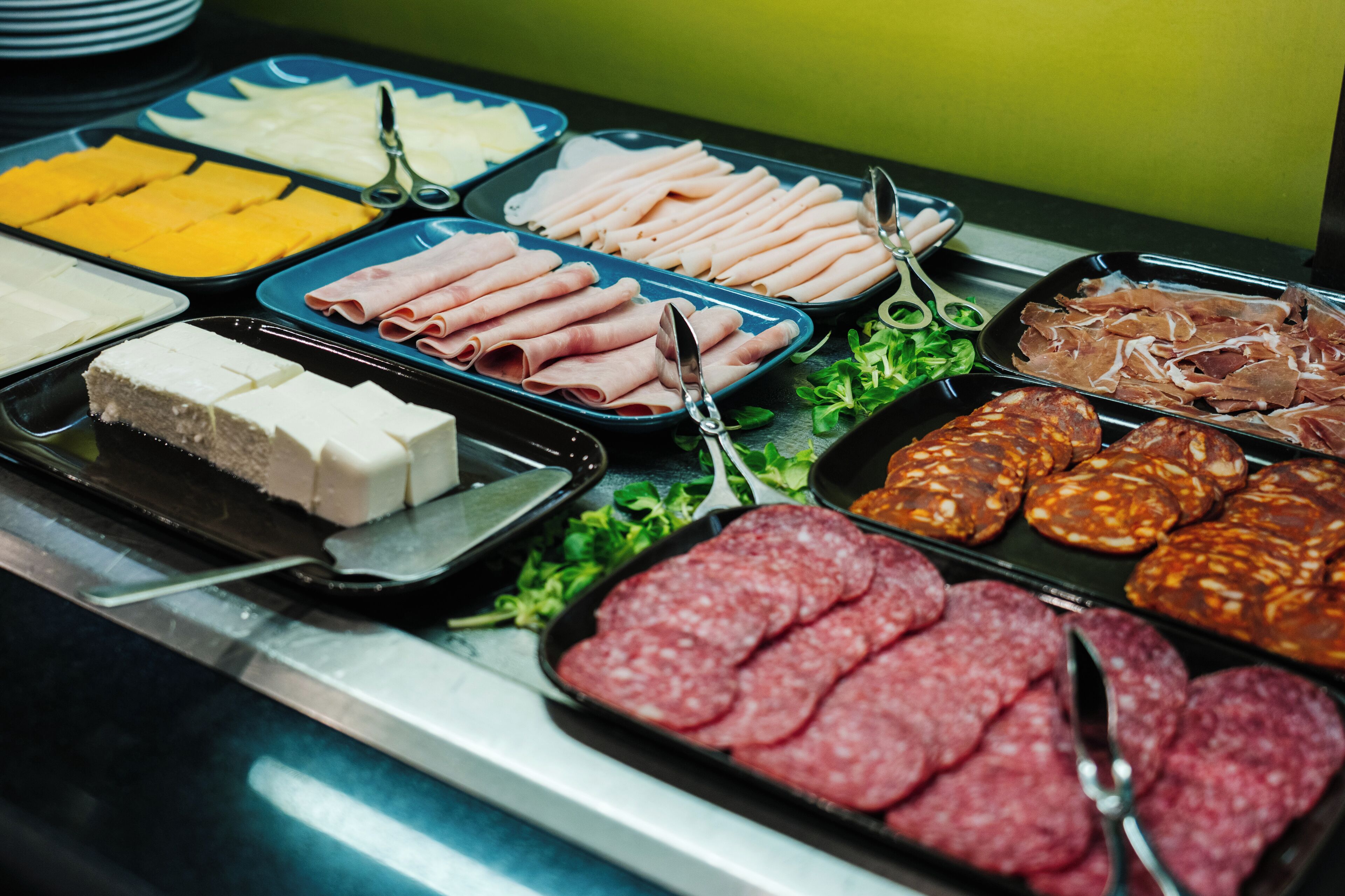 Een buffet met verschillende soorten eten, waaronder vlees, kaas en sneetjes brood.