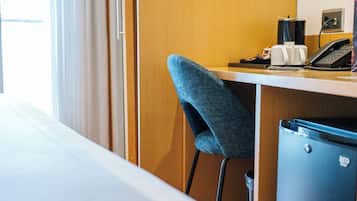 Een hotelkamer met een bed, een bureau met stoel, telefoon en een prullenbak.