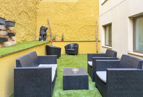 Un espace patio aménagé avec des meubles en osier, une petite statue et des jardinières disposées contre un mur jaune.