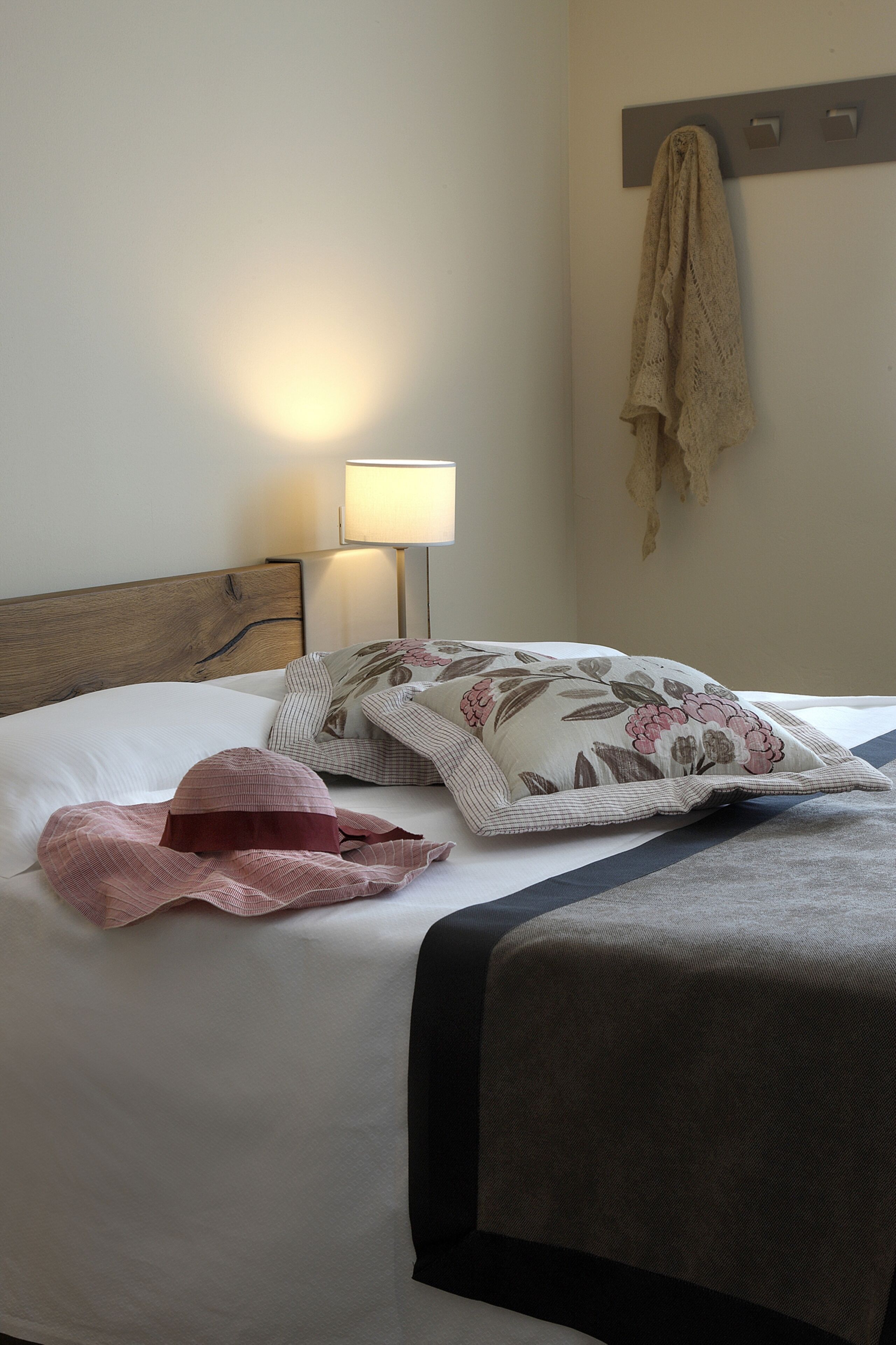 A neatly made bed with a floral pillow, a striped blanket, and a headscarf.
