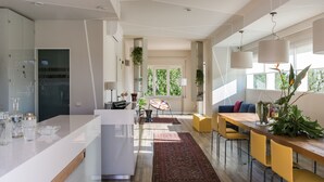 A modern kitchen with a central island, a dining area with yellow chairs, and a large window providing natural light.