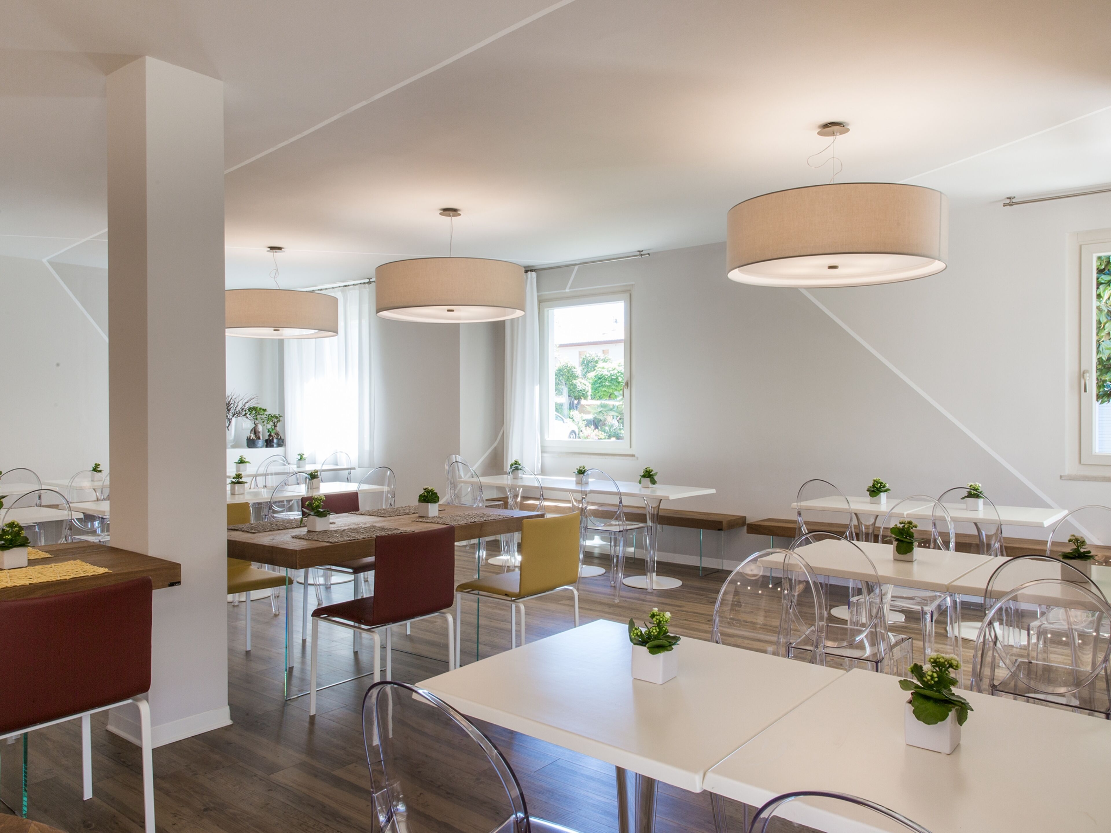 Un comedor moderno con mesas blancas, sillas transparentes y grandes lámparas colgantes.