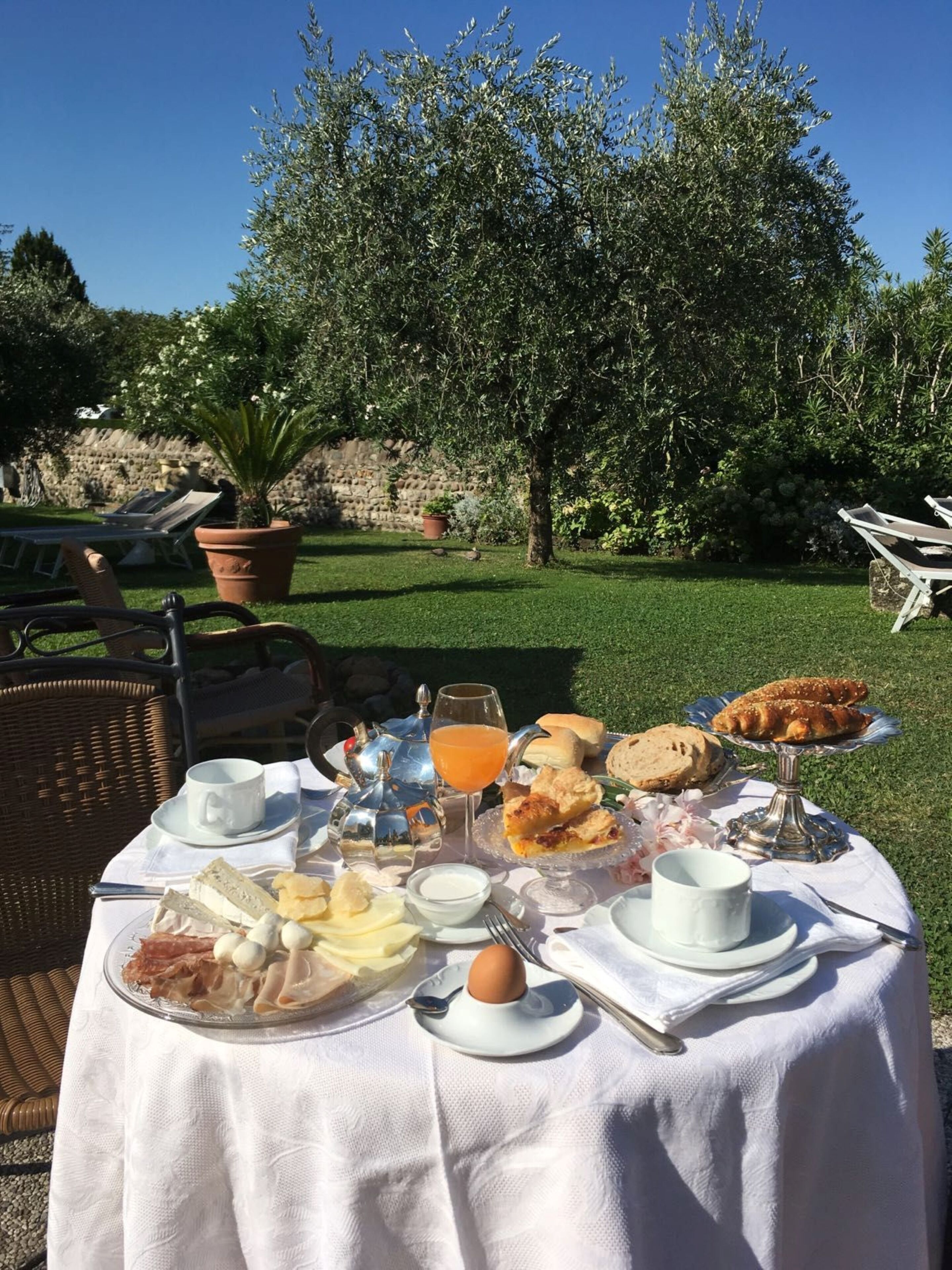 An outdoor dining table set with breakfast items, surrounded by wicker chairs and a stone wall in the background.