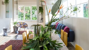 A modern dining area with a wooden table, yellow chairs, and a large potted plant with bird of paradise flowers.