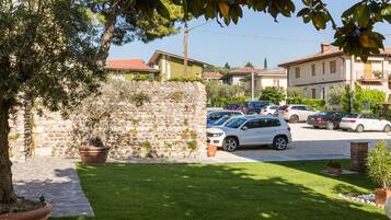 Una strada residenziale con auto parcheggiate, un muro in pietra e un prato curato.