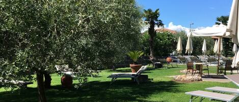 A well-maintained outdoor area with green grass, a large tree, and several lounge chairs and umbrellas.