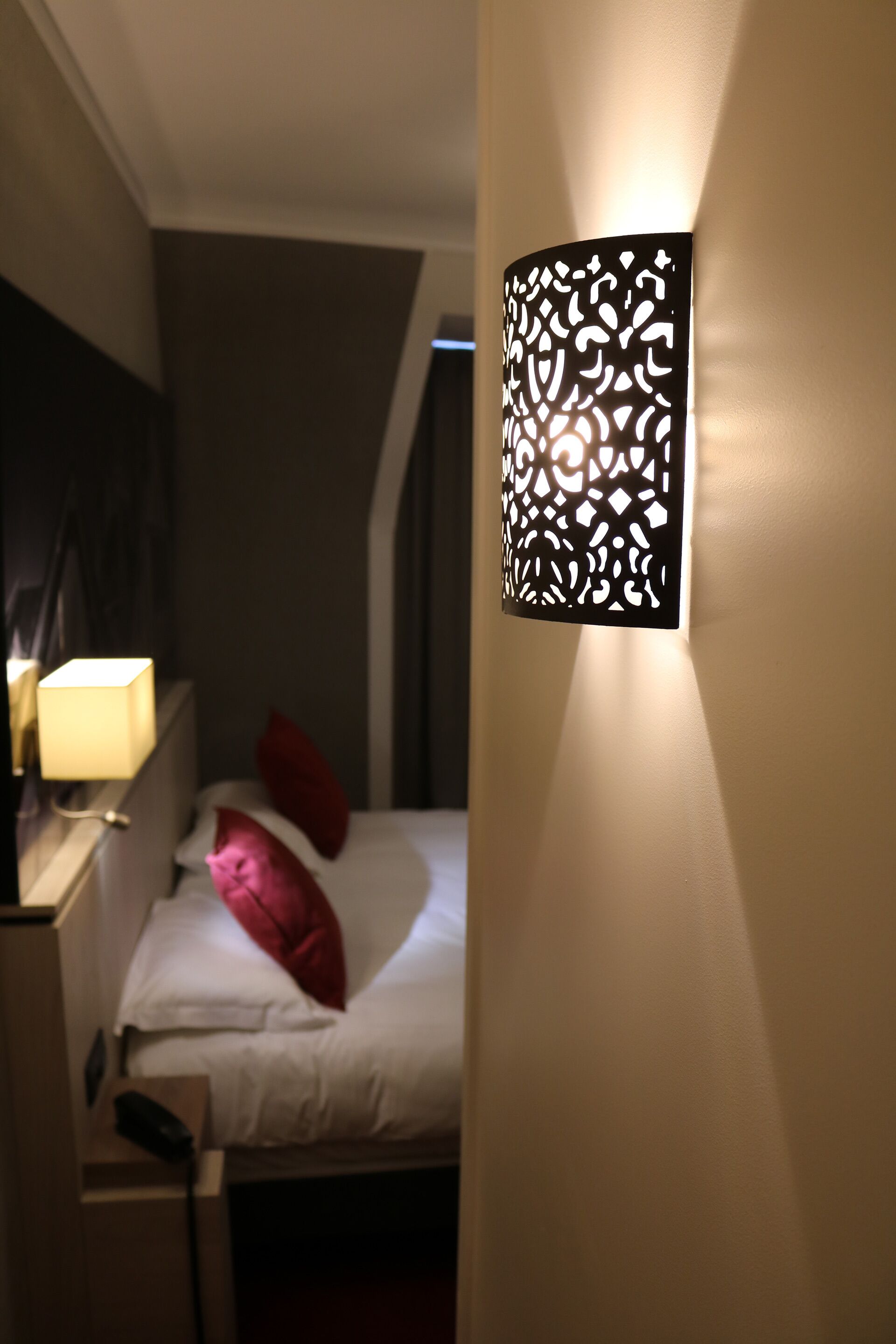Une chambre d’hôtel avec un lit, une table de chevet et un luminaire fixé au mur.
