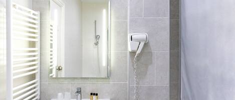 Un baño con lavamanos blanco, espejo y toallero.