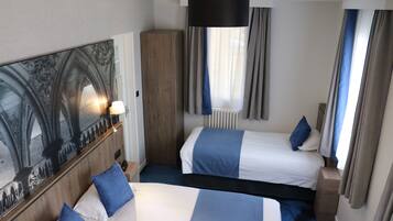 A hotel room with two beds, a large mirror, a wooden wardrobe, and a window with curtains.