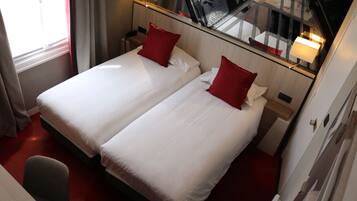 A hotel room with two beds, red pillows, a small desk, and a chair.
