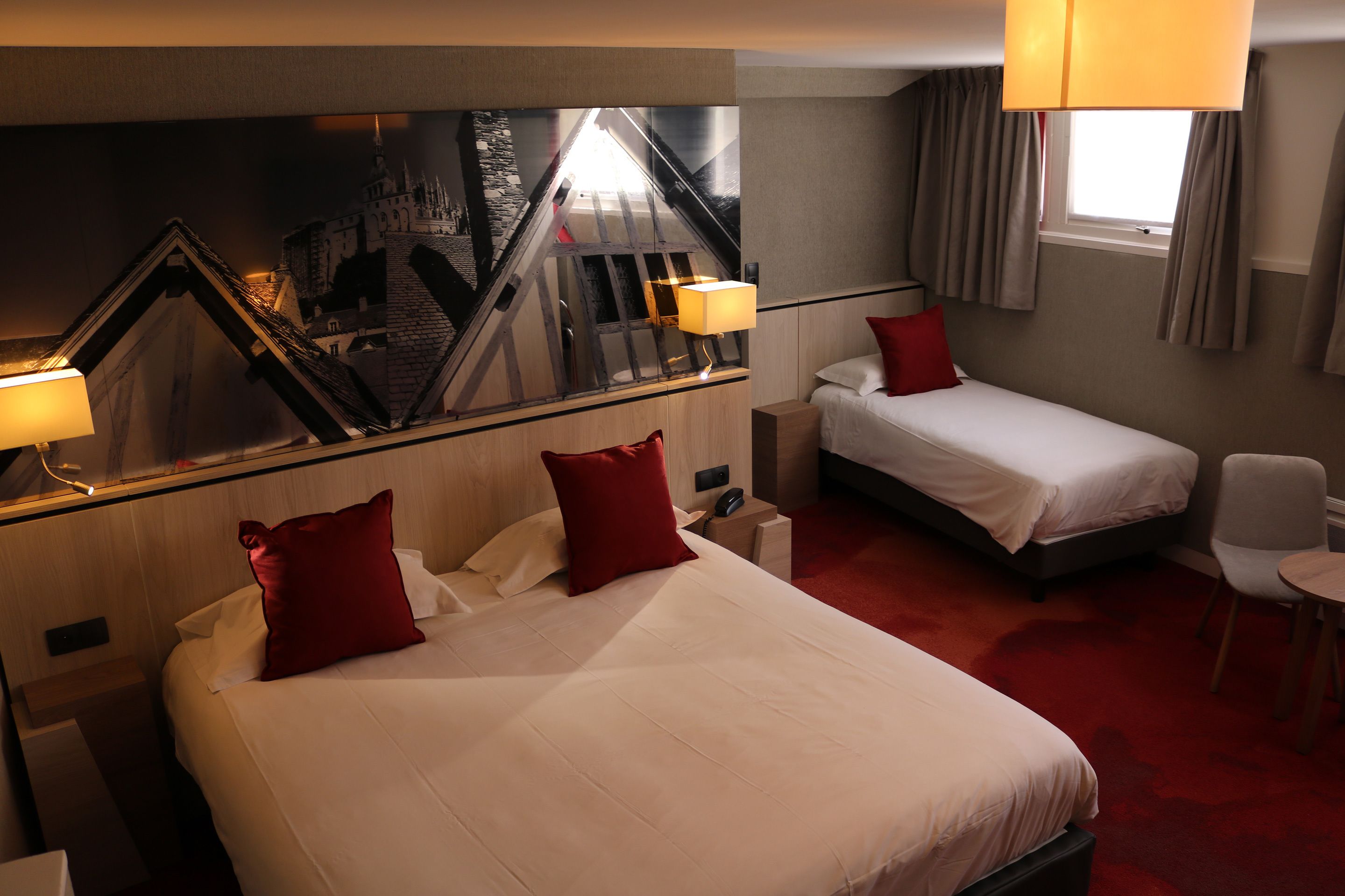 A hotel room with two beds, a mirror, a red carpet, and a window with curtains.