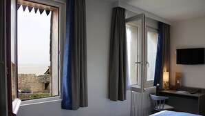 Una habitación de hotel con cama, escritorio, silla, televisión y ventana con cortinas.