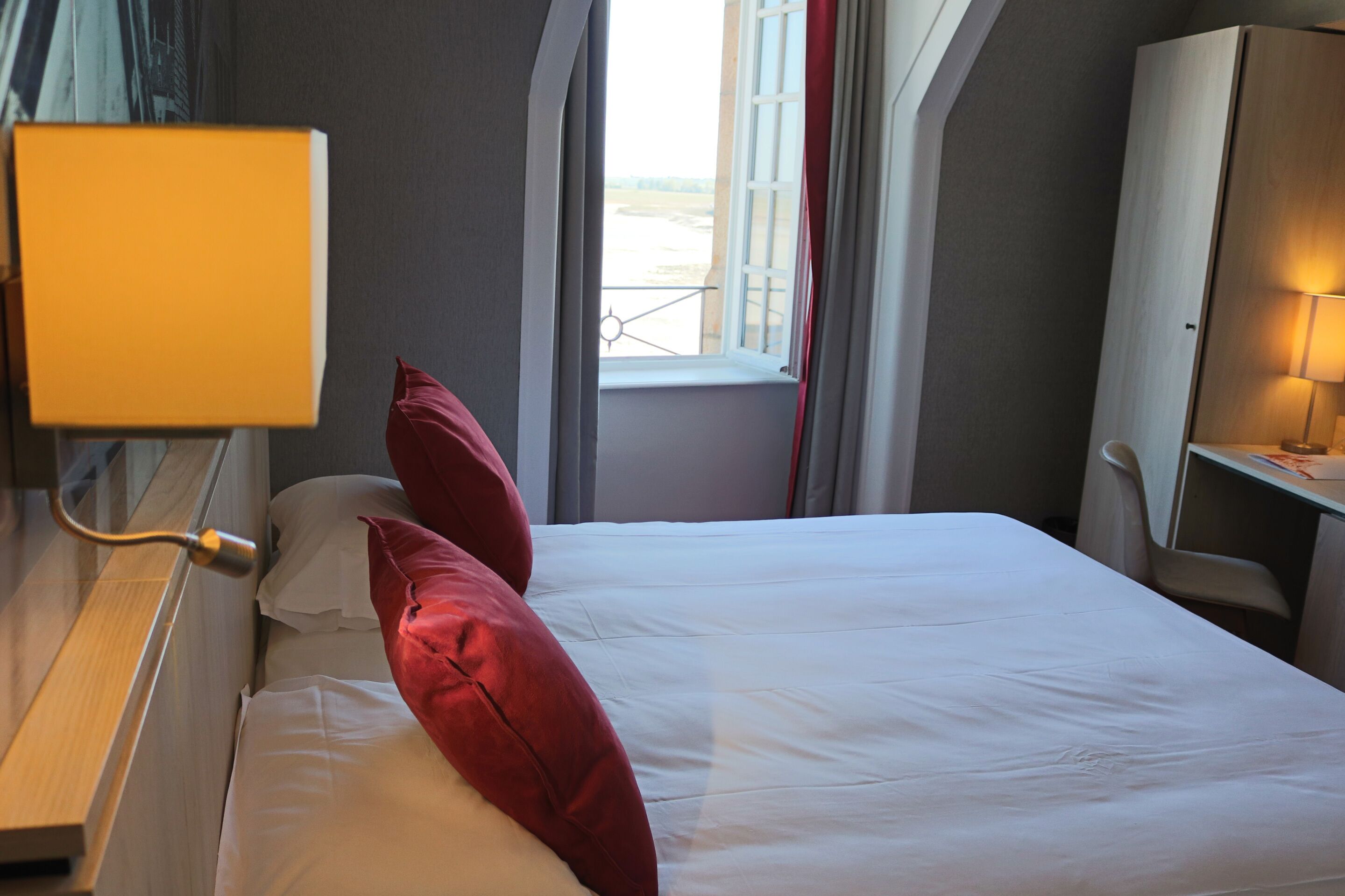 Habitación de hotel con cama, ventana con cortinas, escritorio con lámpara y vista al exterior.