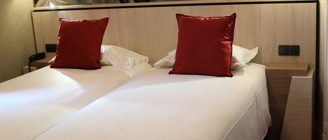 A hotel room with a large bed, two red pillows, a nightstand with a lamp, and a cityscape mural on the wall.