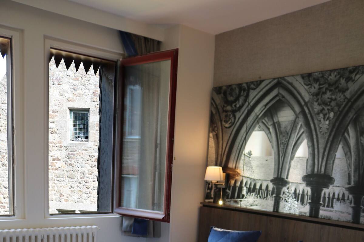 A hotel room with a large bed, a window with curtains, a radiator, and a wall-mounted lamp.