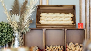 Una exhibición de pan de madera con diversos tipos de pan, una tabla de cortar y un jarrón con plantas secas.
