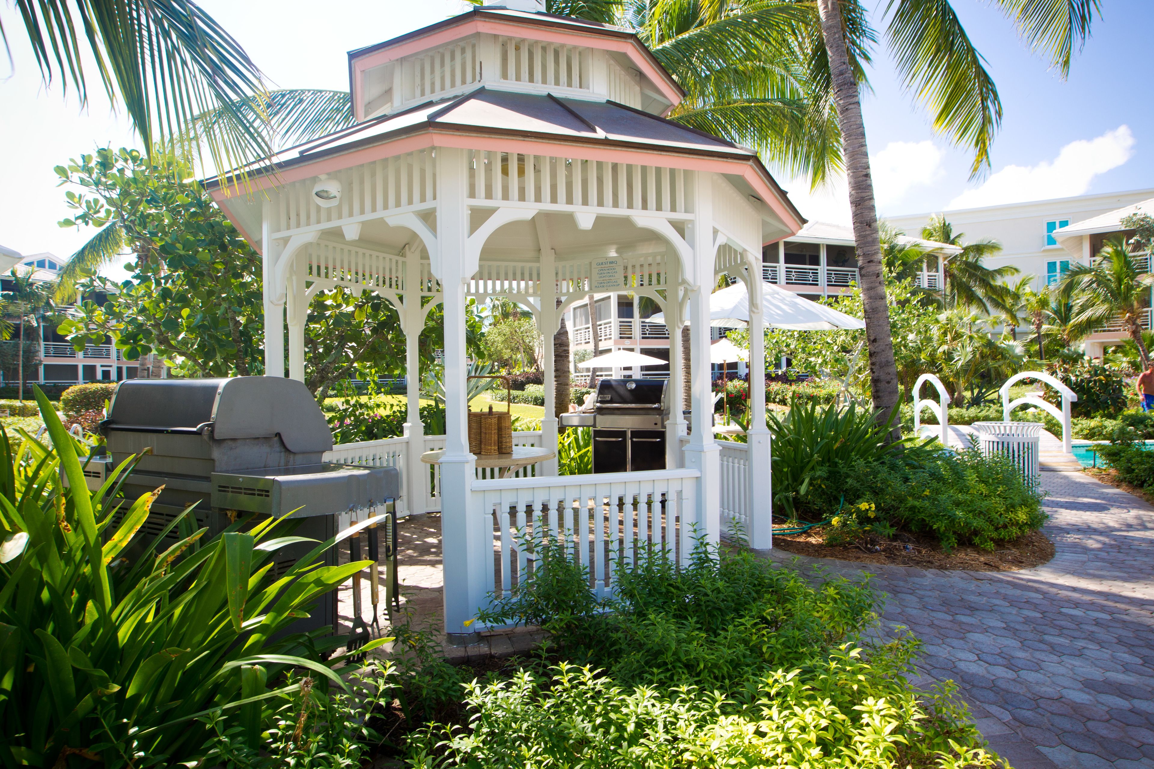 A gazebo with a grill, surrounded by lush greenery and palm trees.