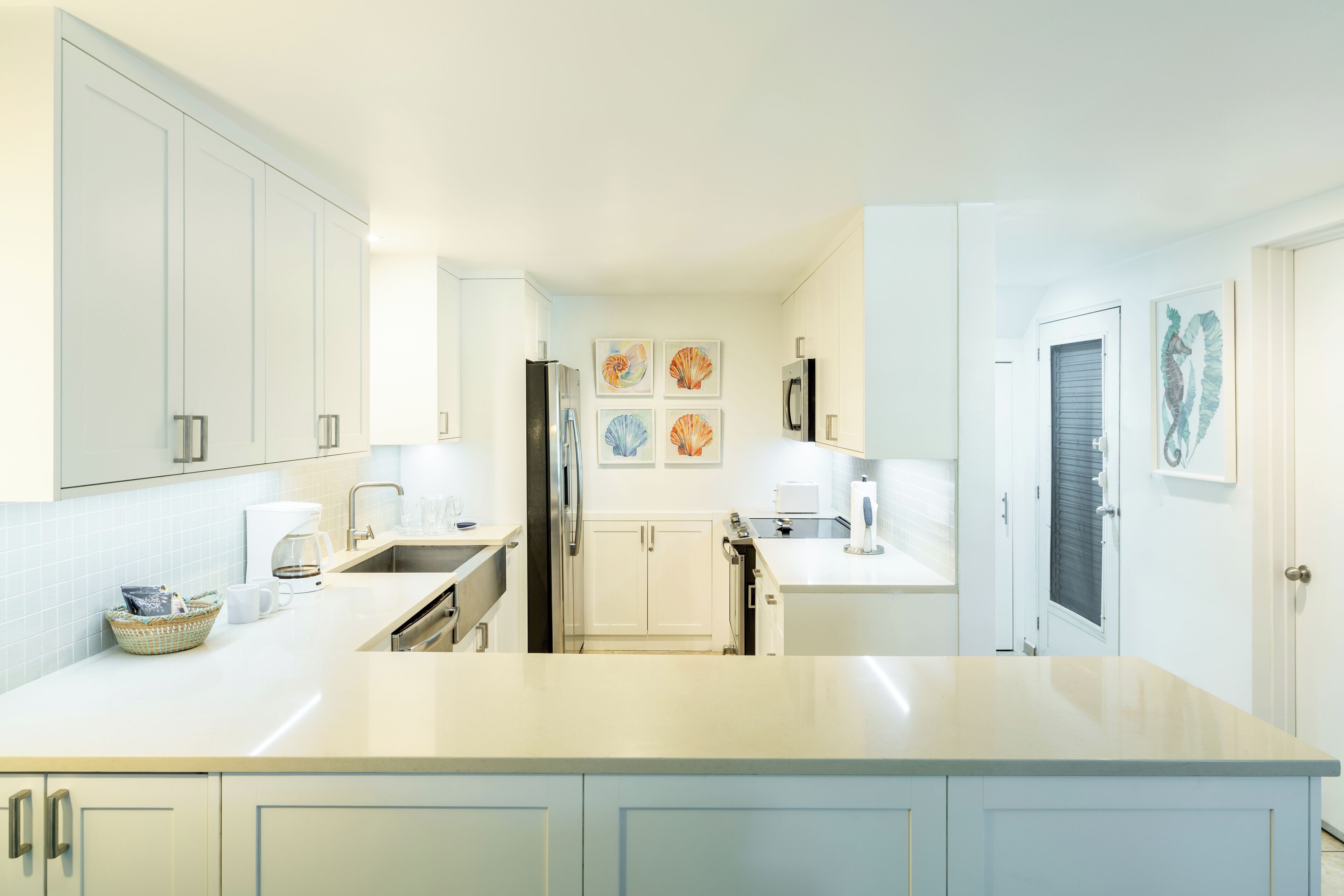 A modern kitchen with white cabinetry, a central island, and artwork on the walls.